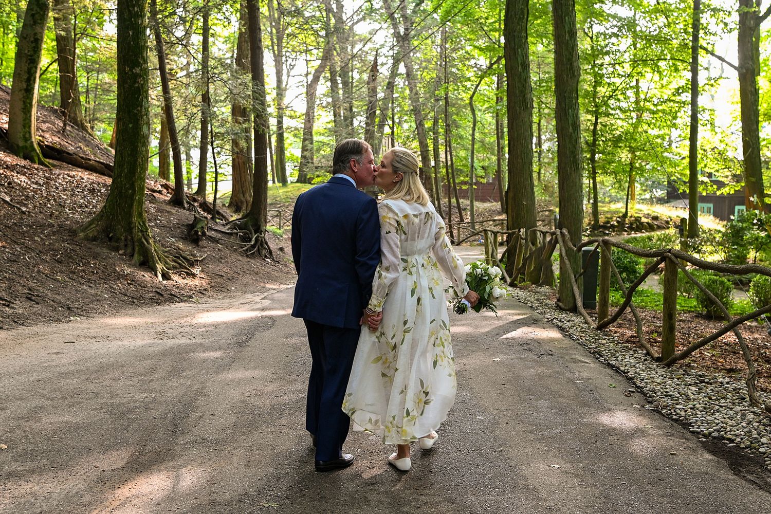 Wedding couple walking together on a forest path surrounded by green trees.