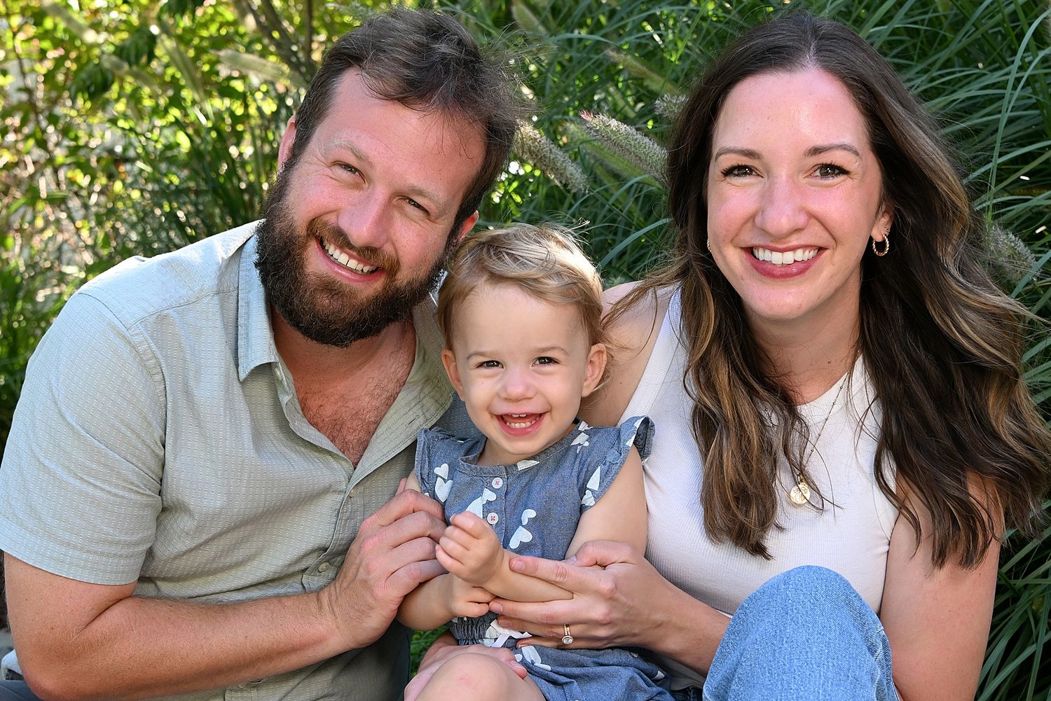 Family portrait session in lush green garden setting during golden hour.