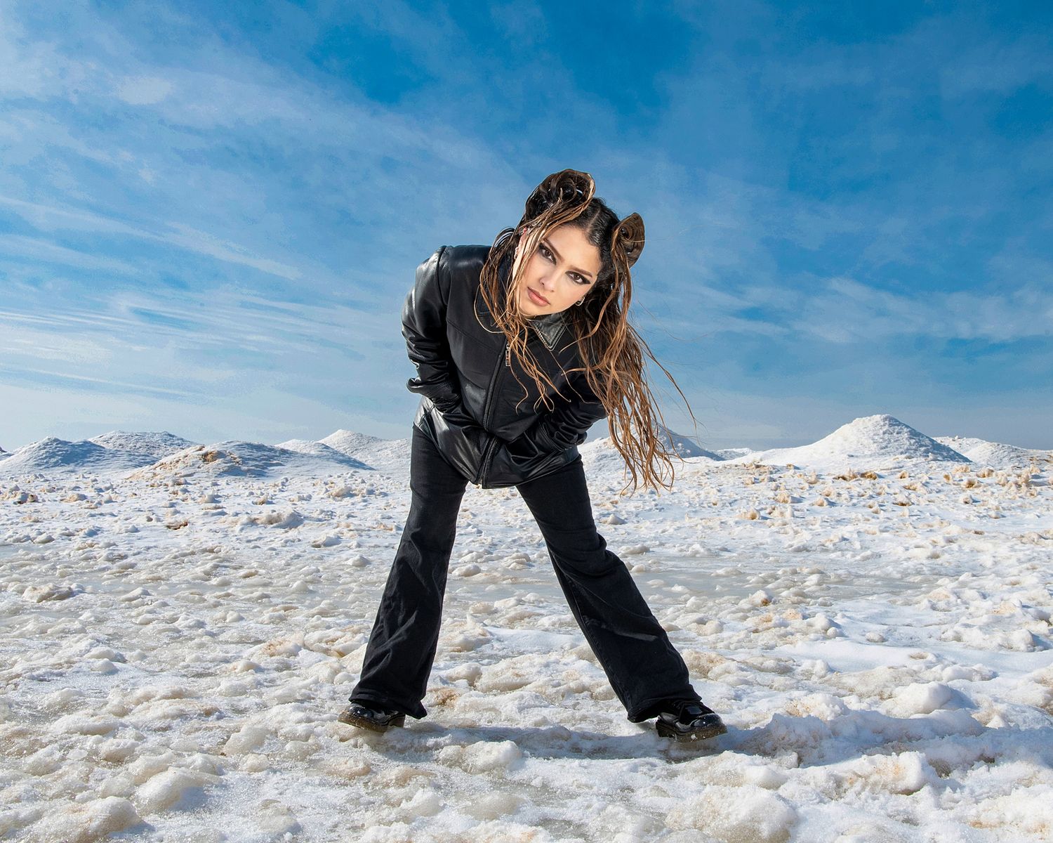 Person in dark clothing making dynamic poses in snowy landscape.