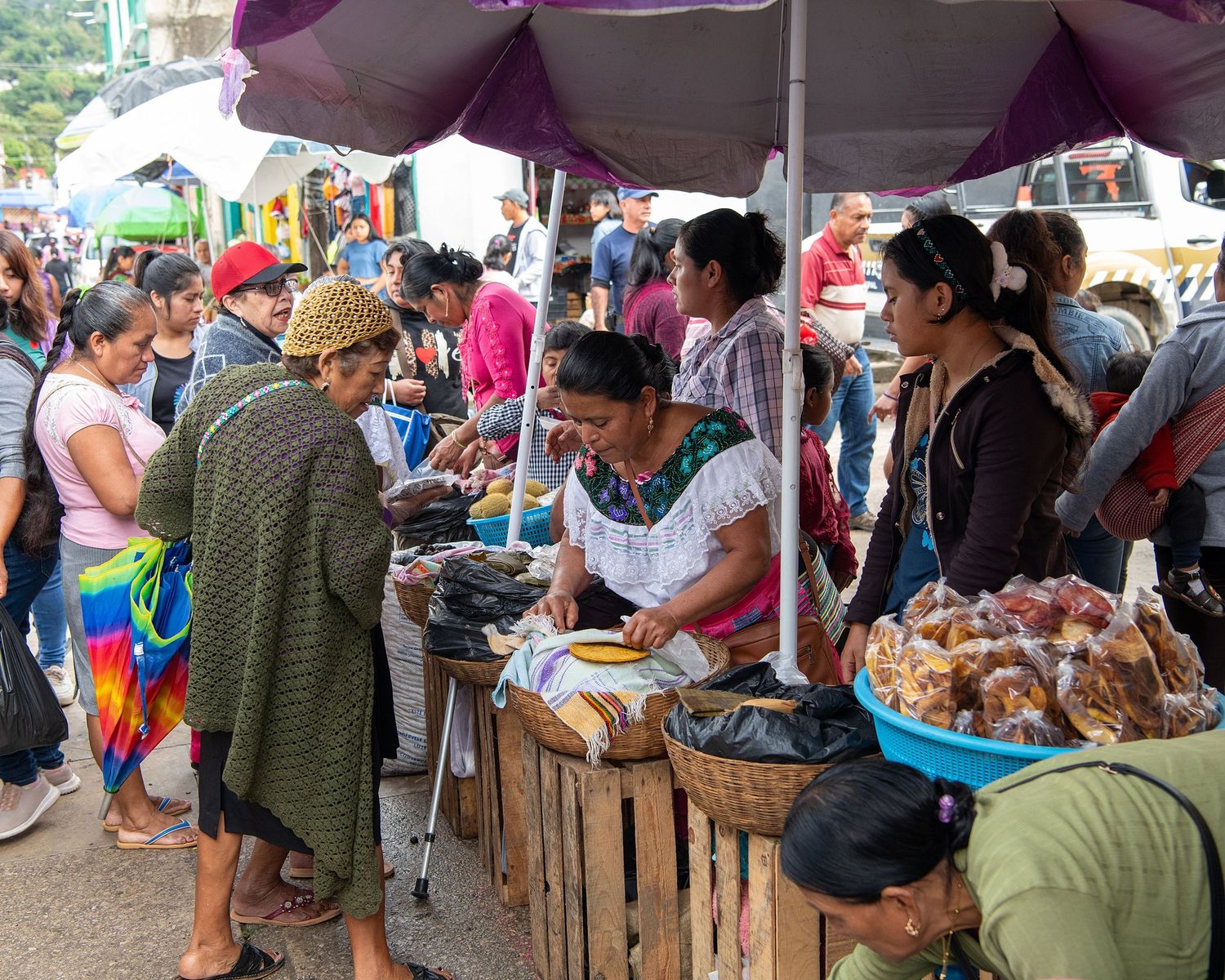 Outdoor market stalls with purple canopies and vendors selling various goods.
