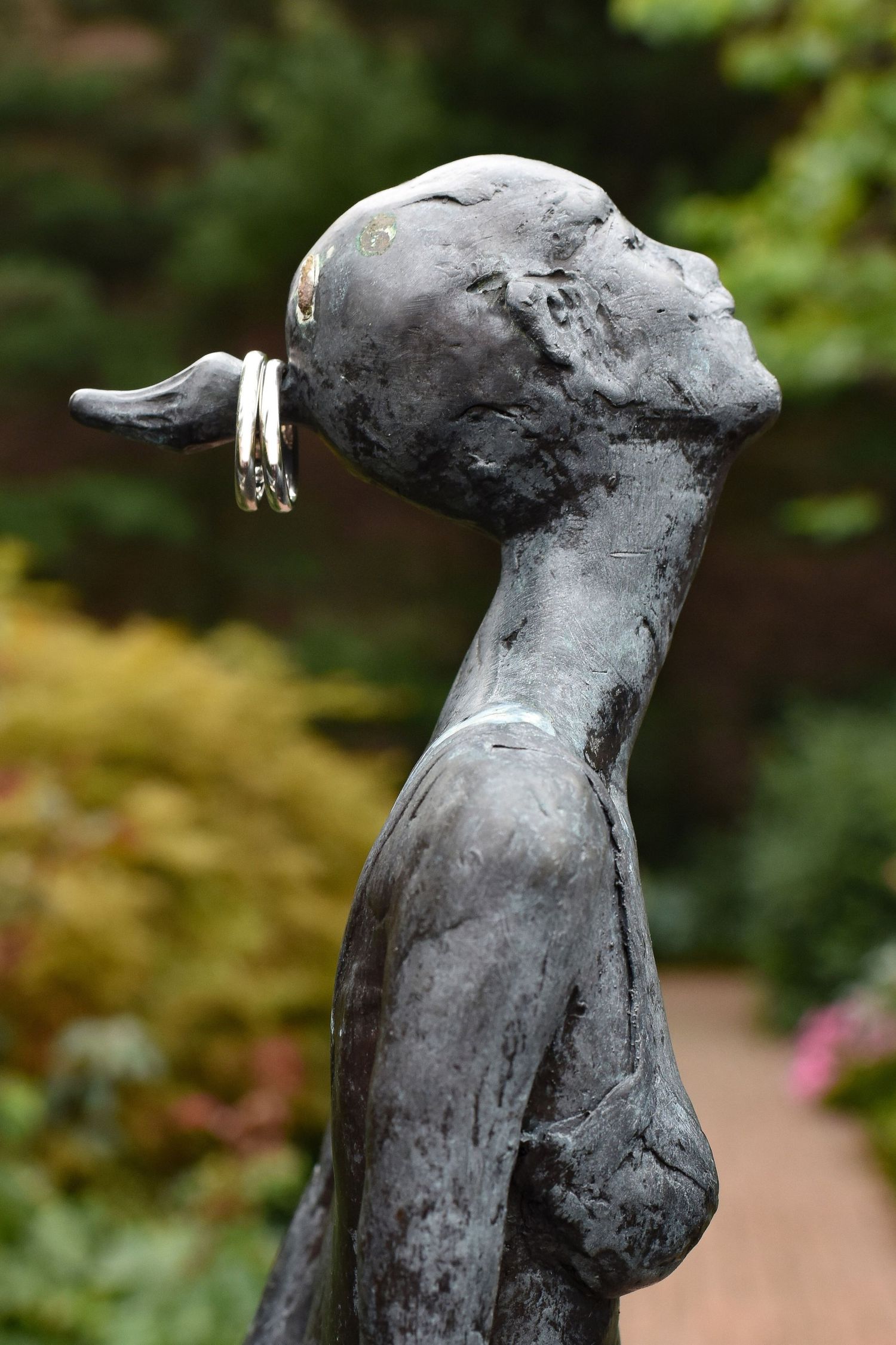 Bronze garden statue with wedding rings hanging from its ear in an outdoor setting.