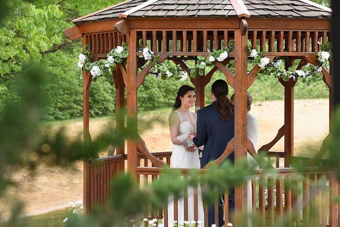 Wedding ceremony setup in a wooden gazebo surrounded by lush green trees and natural scenery.
