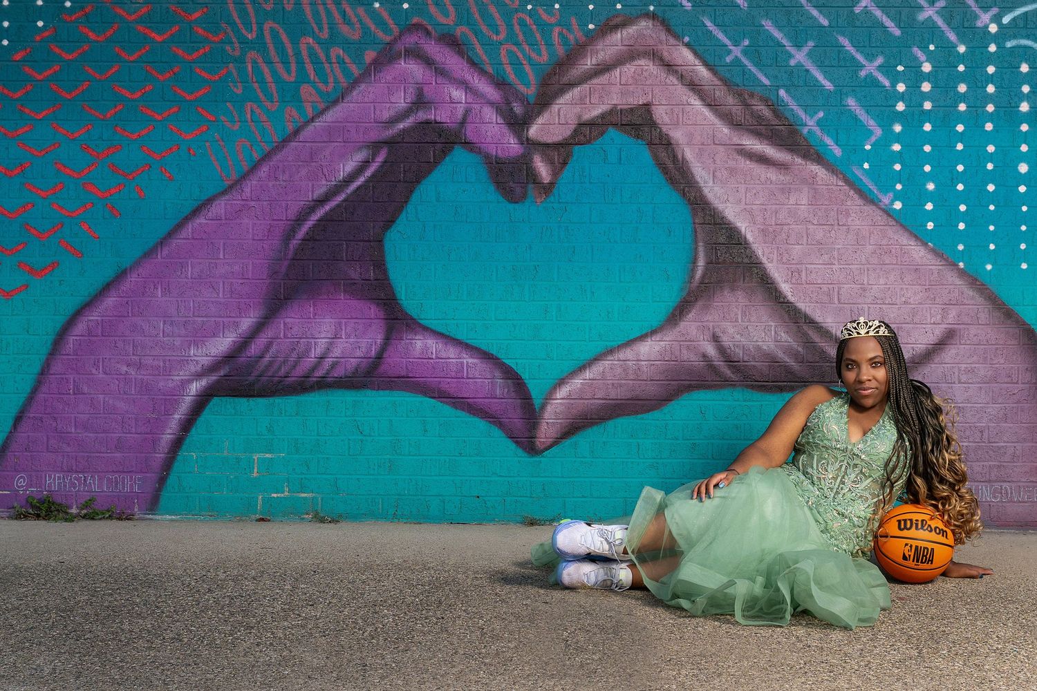 A playful portrait session with heart hand gestures against a teal and purple mural background.