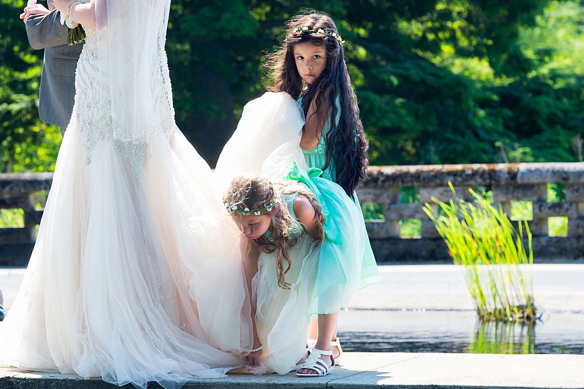 Wedding photo session by a pond with bride in flowing white dress among natural greenery.