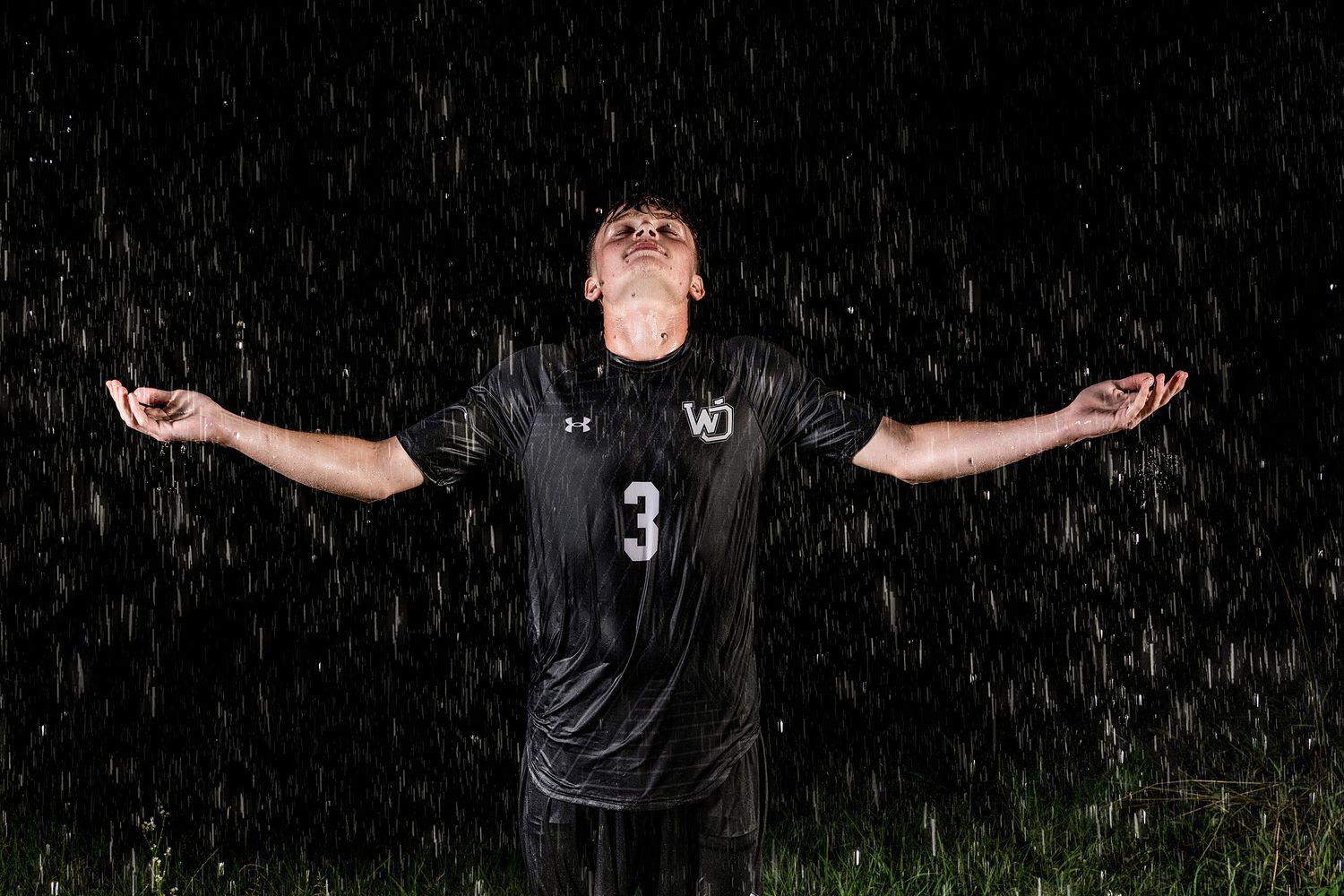 Soccer player practicing in the rain with arms outstretched.