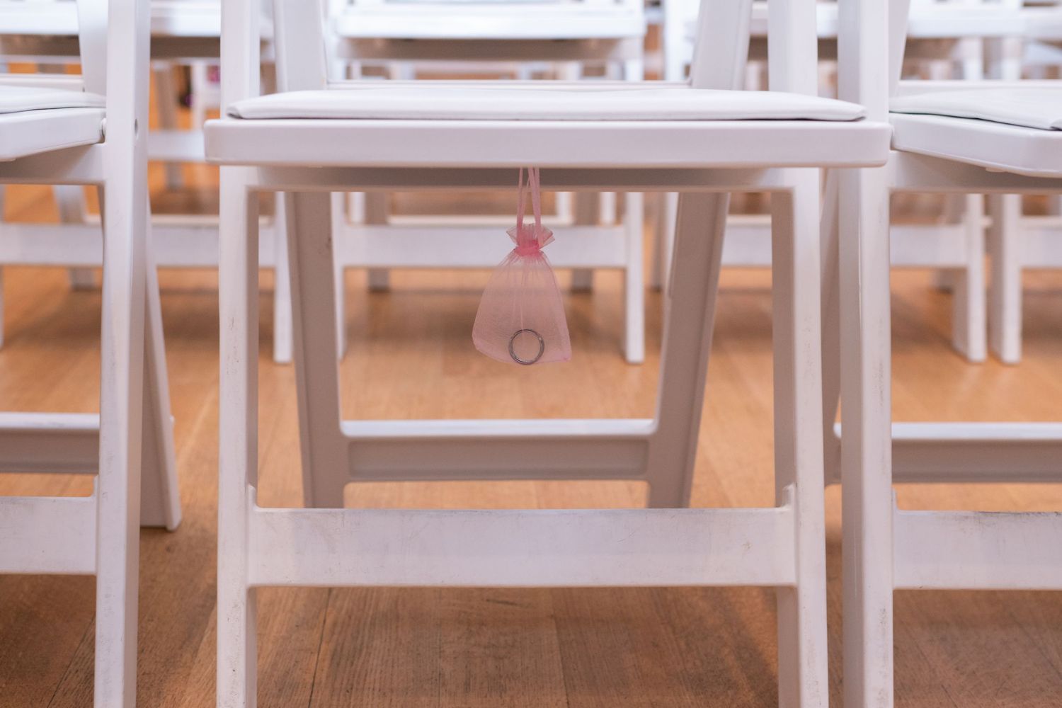White wooden chairs arranged in rows on hardwood floor, with a pink tag hanging from one chair.