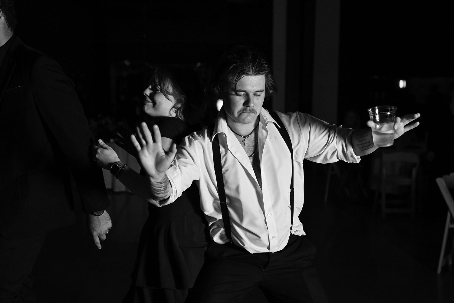 Groom dances energetically with arms outstretched in black and white wedding reception photo.