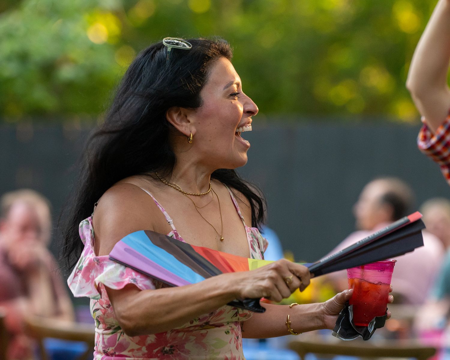 A joyful attendee in a floral dress holds flags while celebrating at an outdoor summer event.