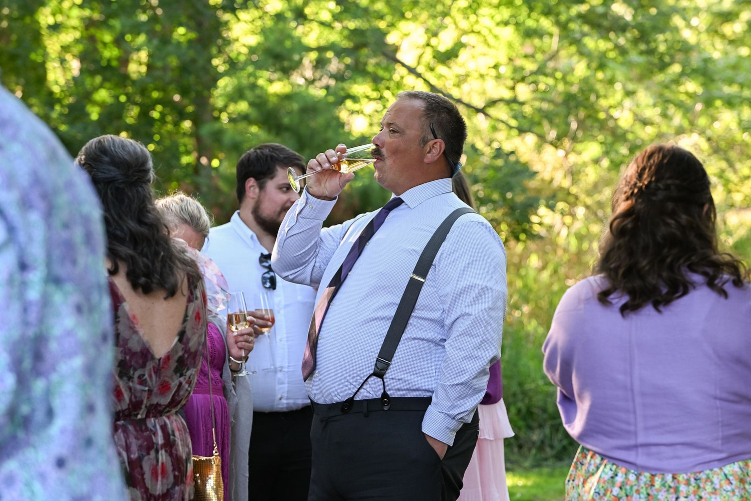 Guests mingle and socialize at an elegant outdoor garden party with lush greenery in the background.