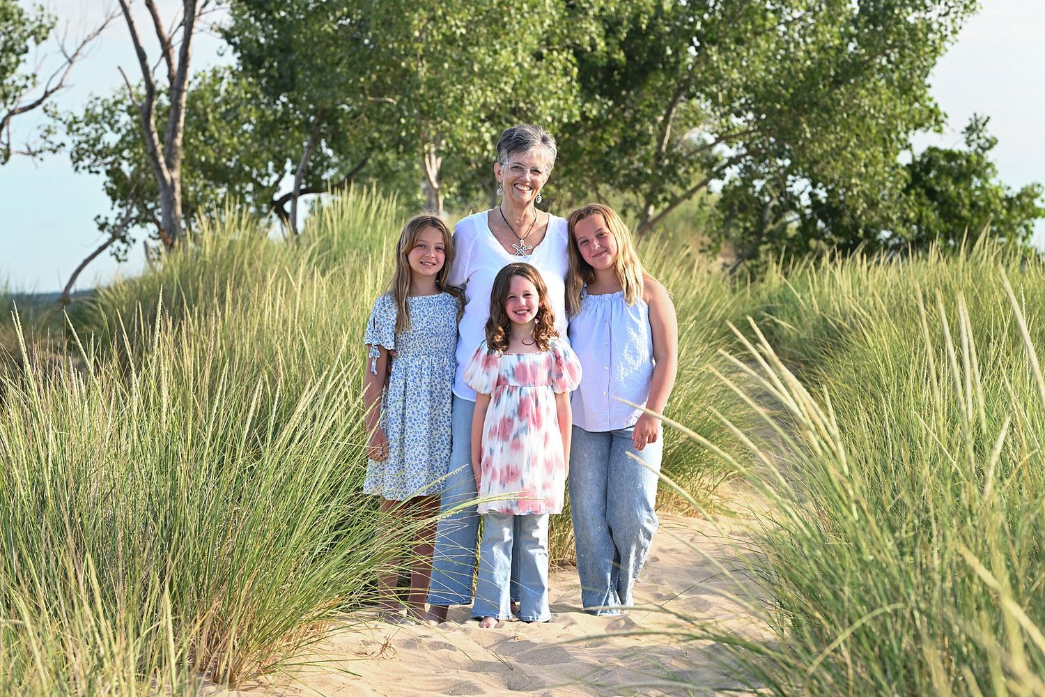 Family walking together along a scenic beach path with tall grass and trees.
