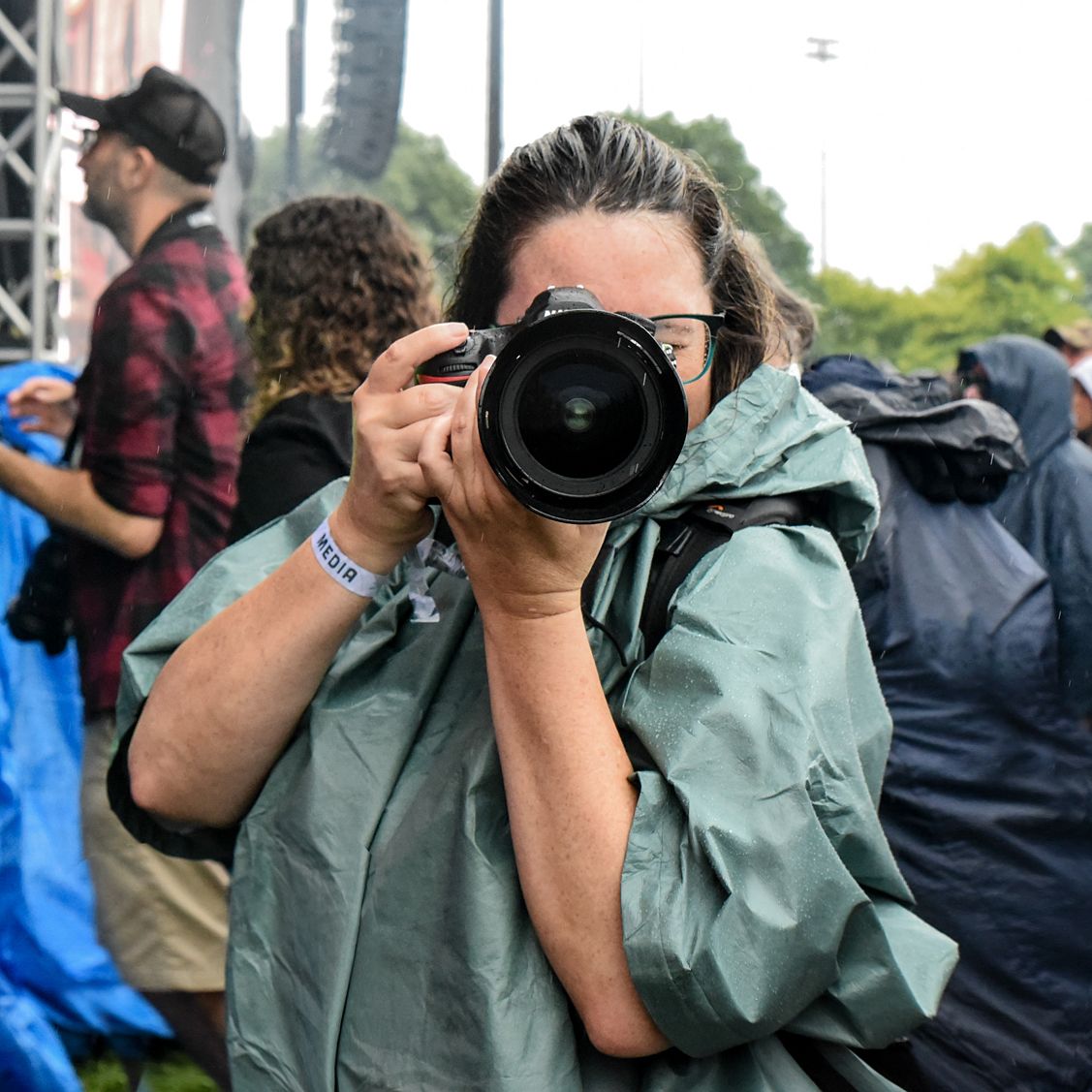 A photographer in a green rain jacket captures photos at an outdoor event.