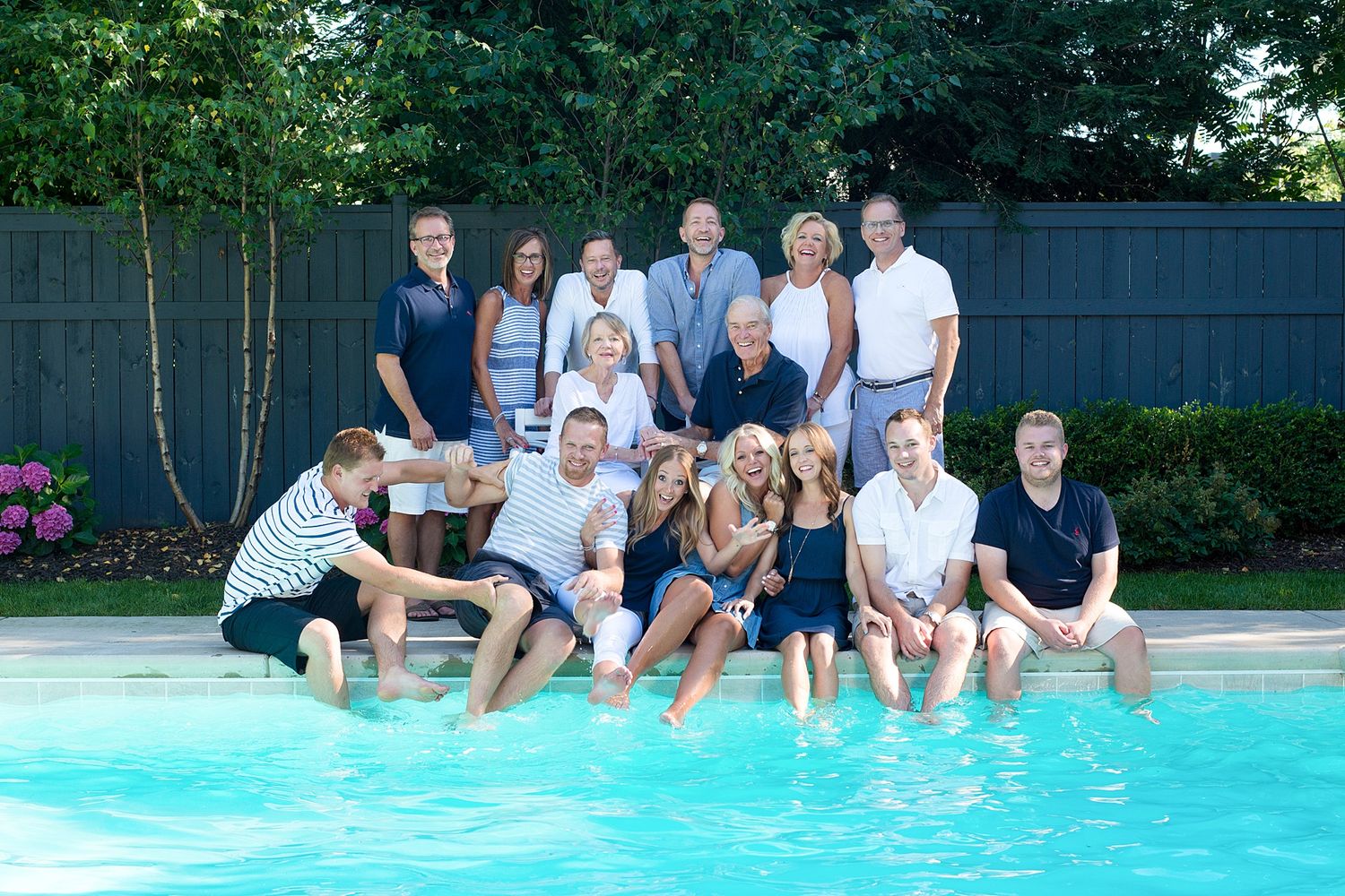 Large group gathered around a swimming pool on a sunny summer day.