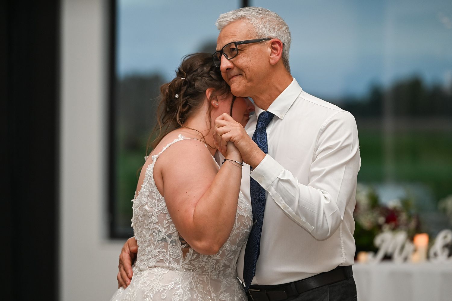Father and bride share an emotional first dance at an indoor wedding reception.