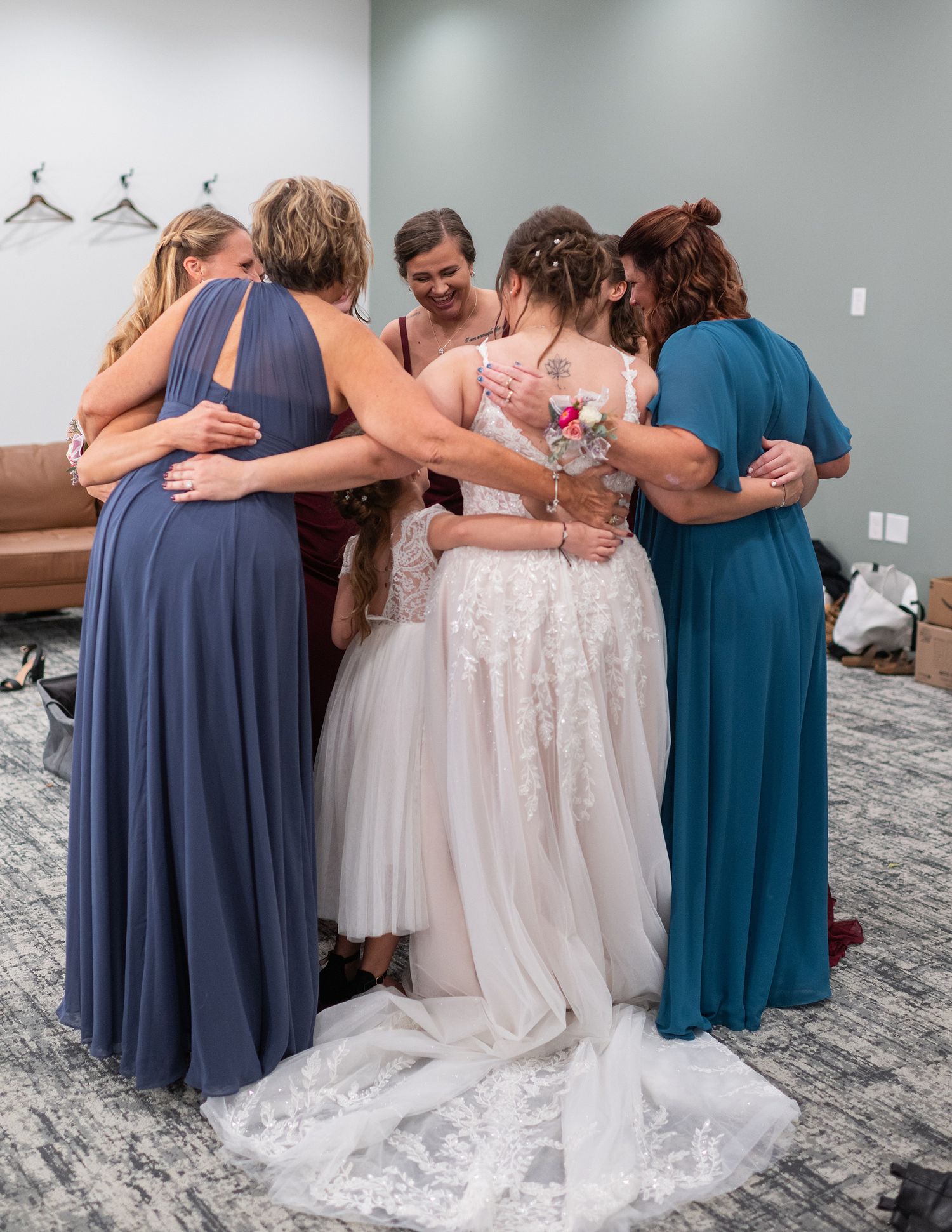 Bride and bridesmaids share a group hug in dressing room before wedding ceremony.