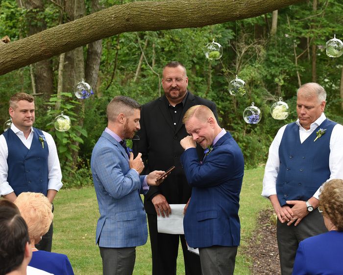 Emotional outdoor wedding ceremony under a tree with hanging glass decorations.
