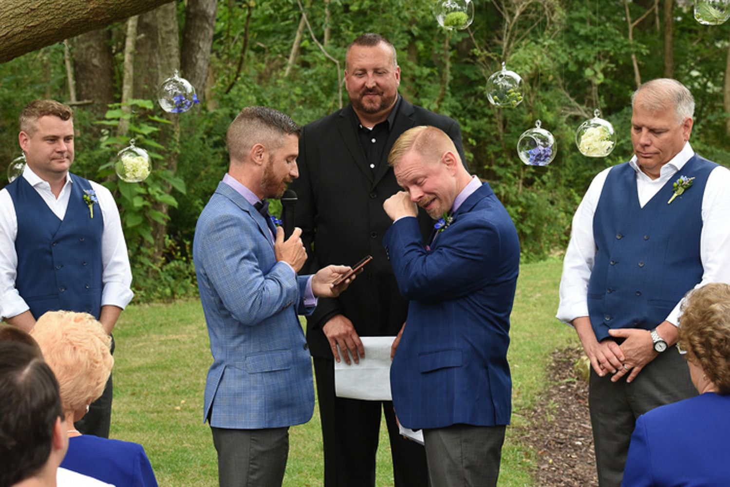 Groomsmen in navy suits celebrating outdoors with bubbles floating in the air.