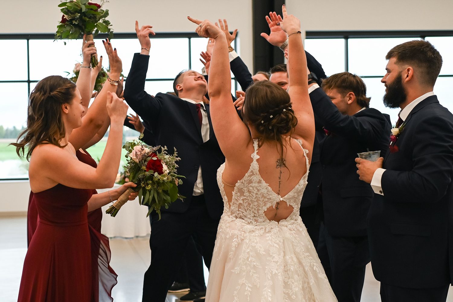 Bride in lace gown celebrating with bridesmaids and groomsmen at joyful wedding reception.
