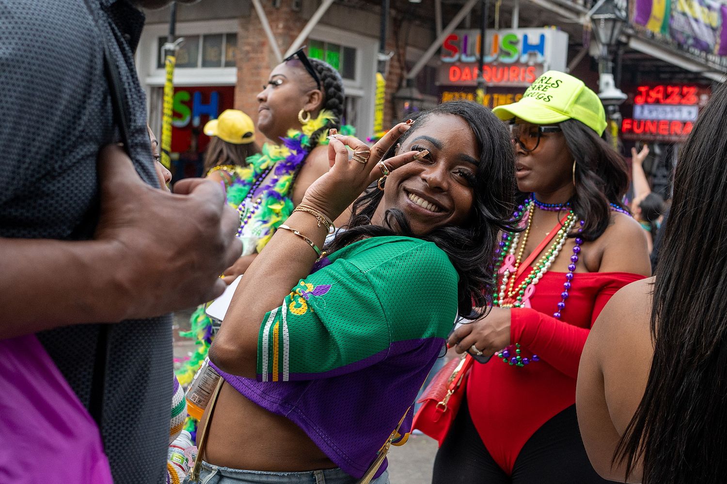 Revelers in bright green outfits catch beads from balconies during New Orleans Mardi Gras celebration.