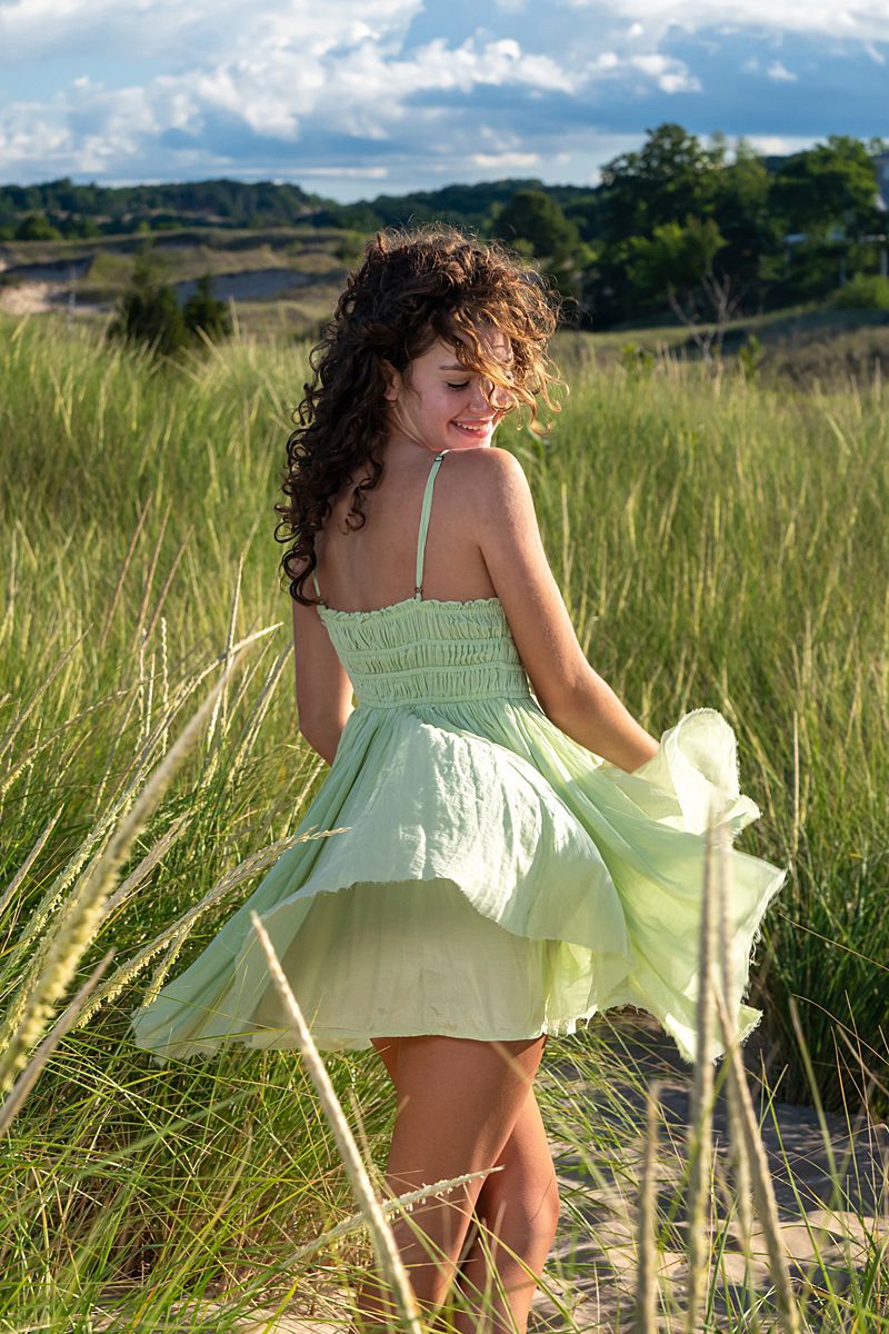 A flowing mint dress catches sunlight in a summer meadow with mountains in the distance.