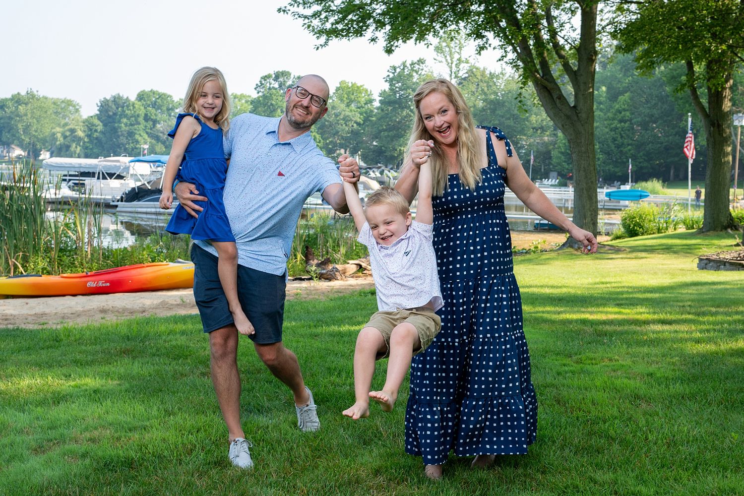 Playful outdoor family photos taken in a grassy park setting near water.