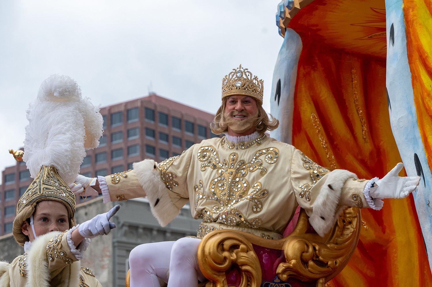 Ornate parade float decorated in gold and white moving through an urban setting.