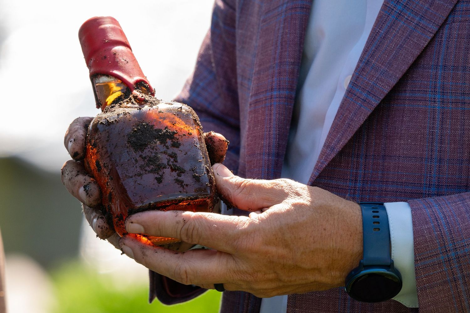Hands holding a decorative bottle of aged liquor in sunlight while wearing a plaid jacket.
