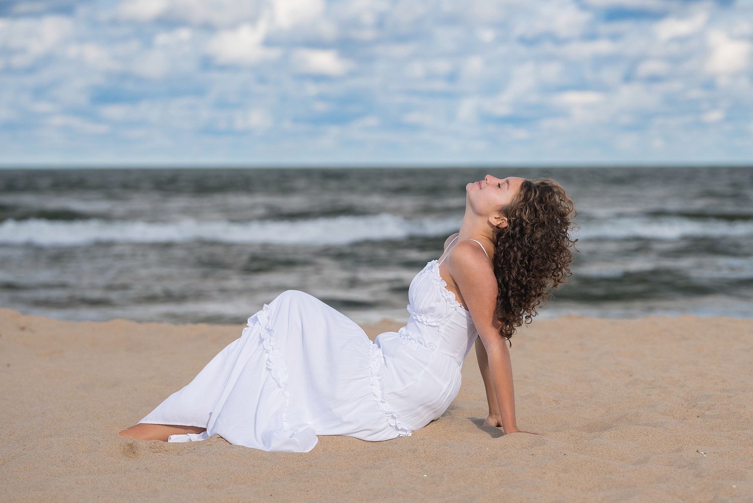 Woman in white dress lying on sandy beach with ocean waves in background.