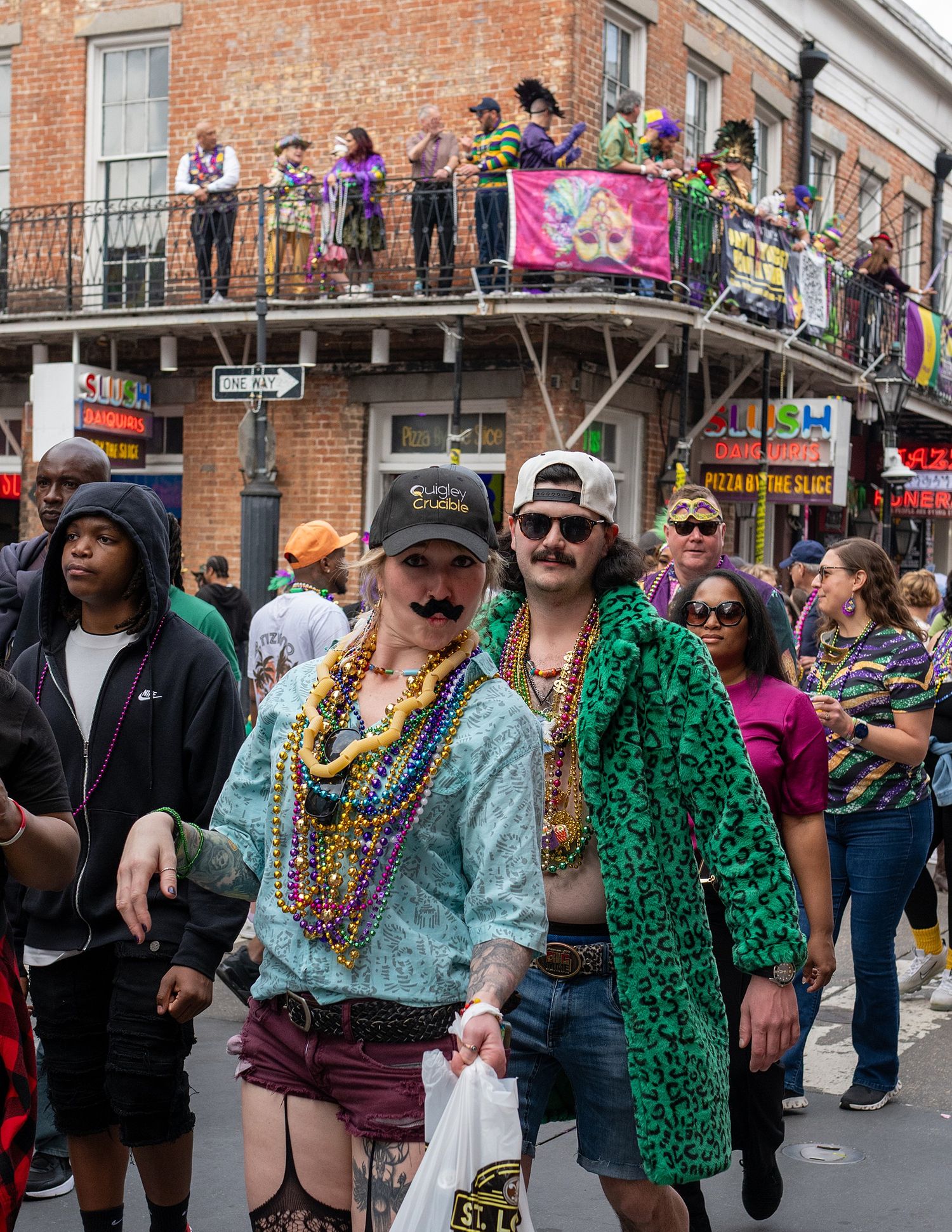 Festive crowd celebrates on Bourbon Street during Mardi Gras with colorful beads and costumes.