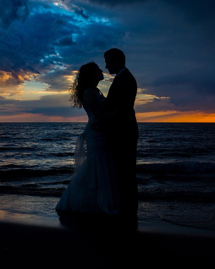 Silhouettes of a couple embracing on the beach at sunset with dramatic ocean waves.