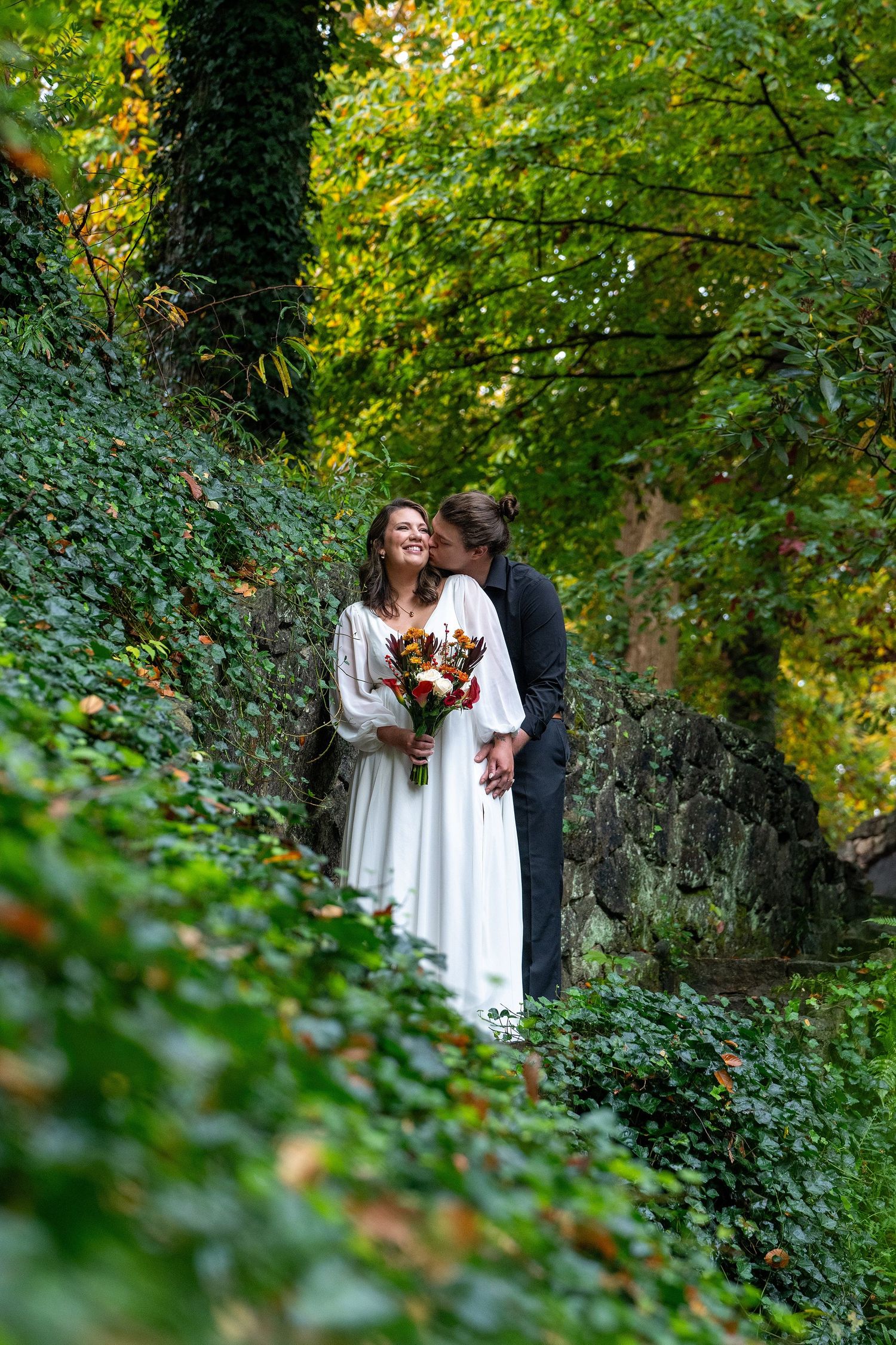 Wedding couple in romantic garden setting surrounded by lush green ivy and trees.