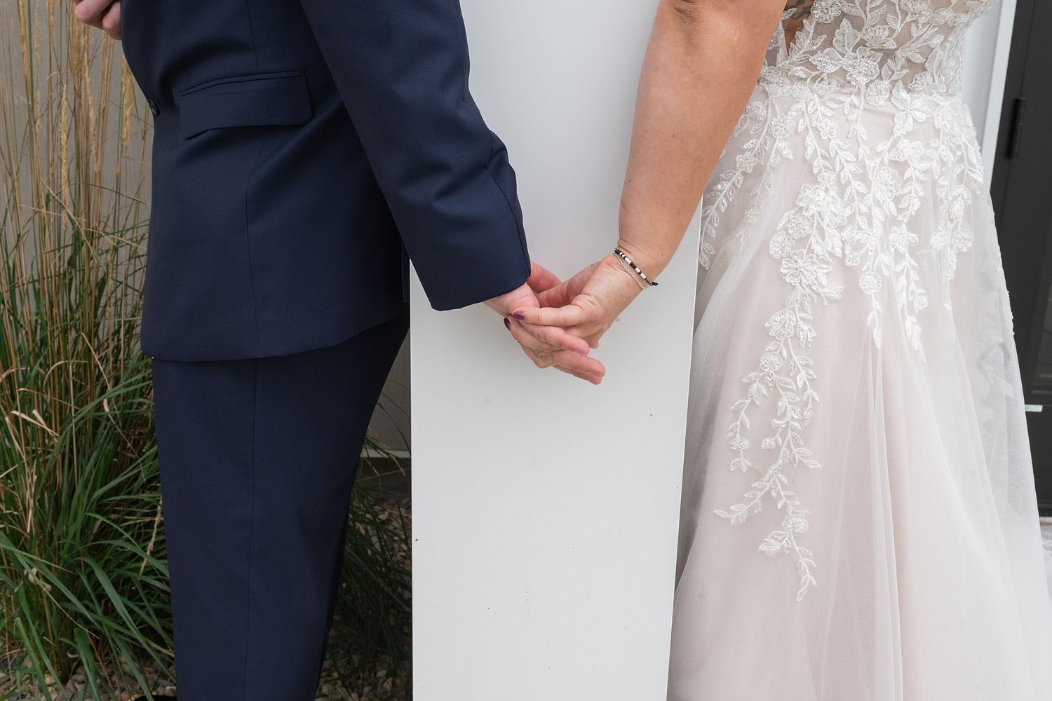 Bride and groom holding hands in wedding attire outside.