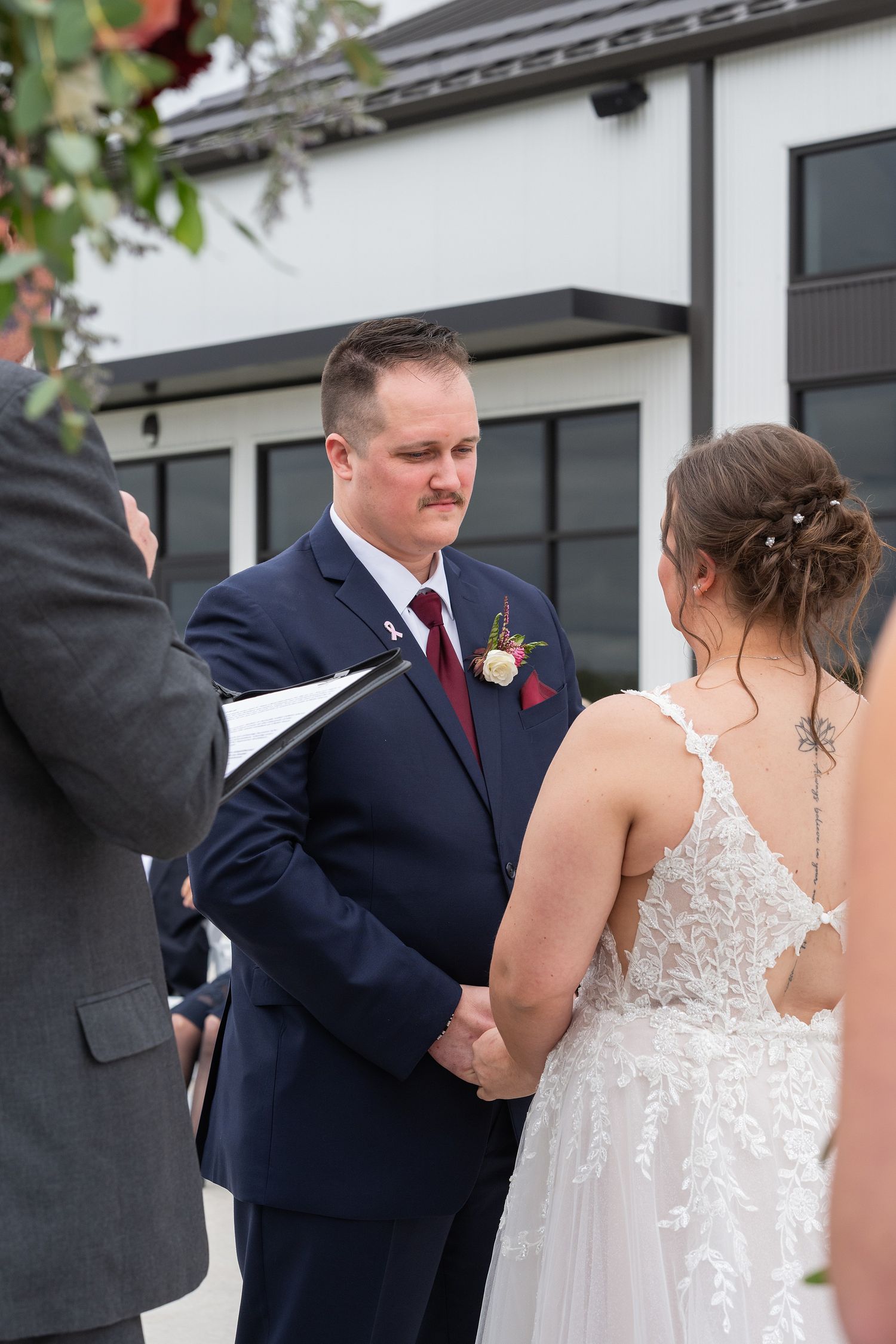 Groom in navy suit holds brides hands during outdoor wedding ceremony vows.