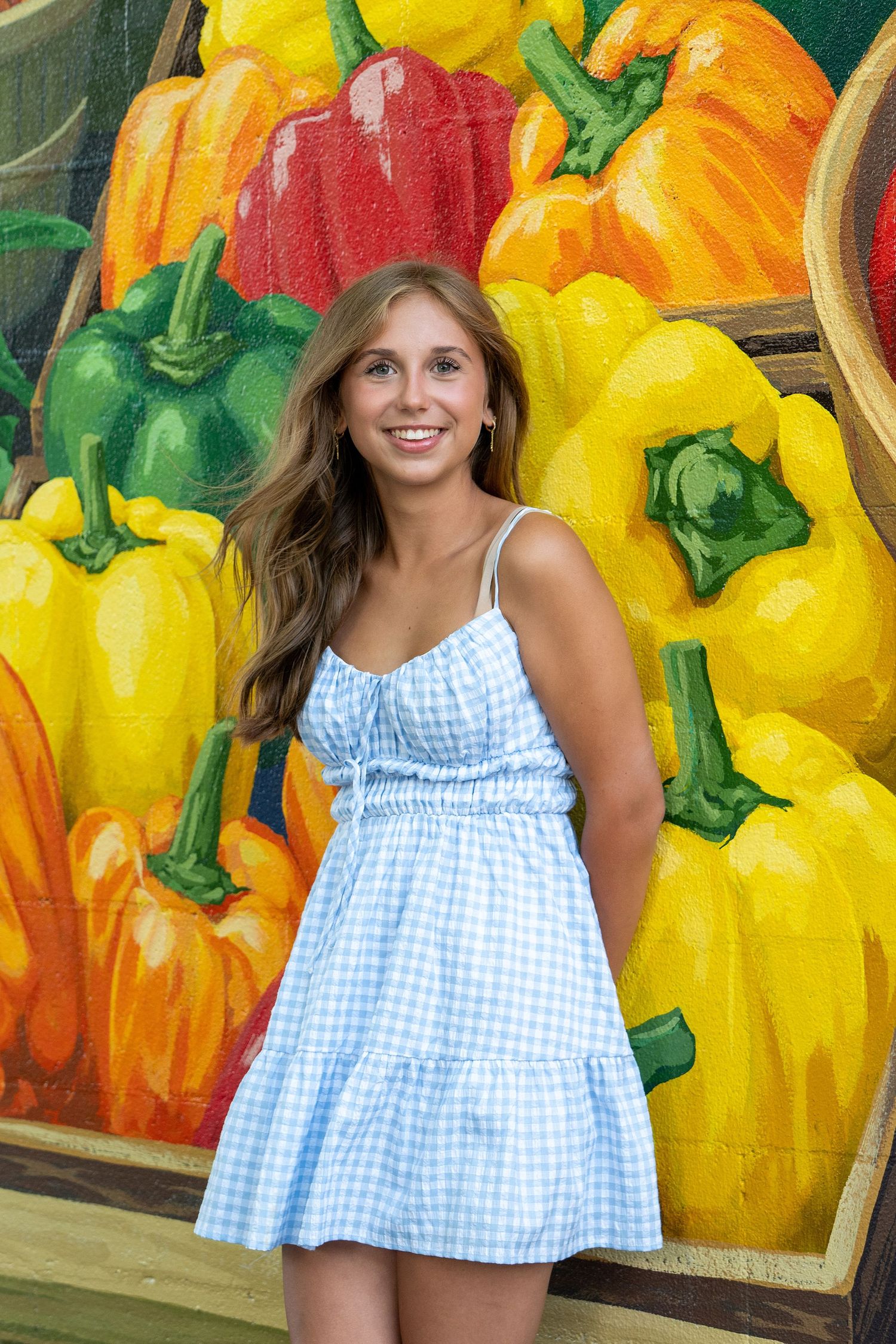 Blue gingham dress against colorful wall mural of vibrant yellow and orange peppers.