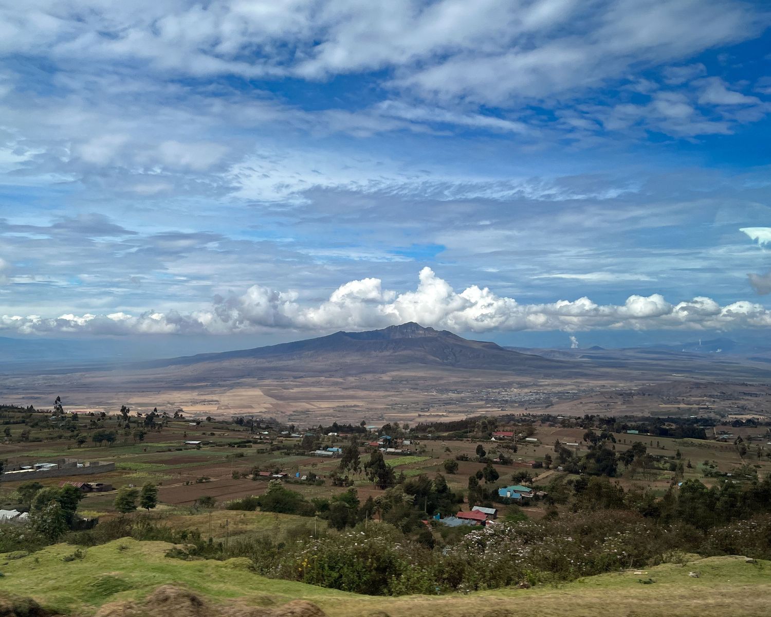 Panoramic view of rolling hills and mountains under a dramatic blue sky with white clouds.