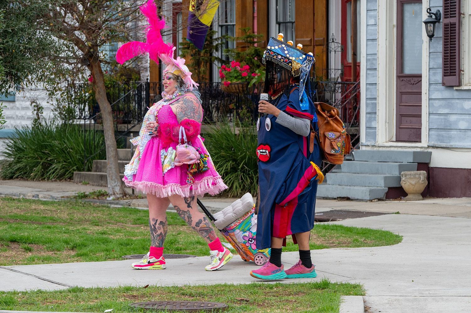 Two colorfully dressed carnival performers in bright costumes interact on a residential sidewalk.