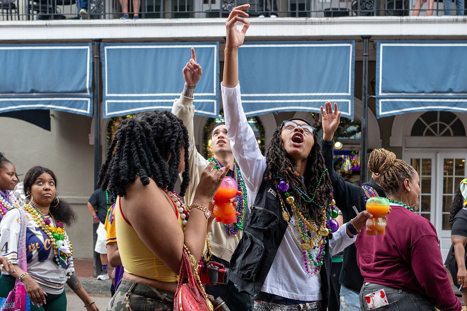 Enthusiastic crowd celebrating beneath decorated balconies during Mardi Gras festivities.