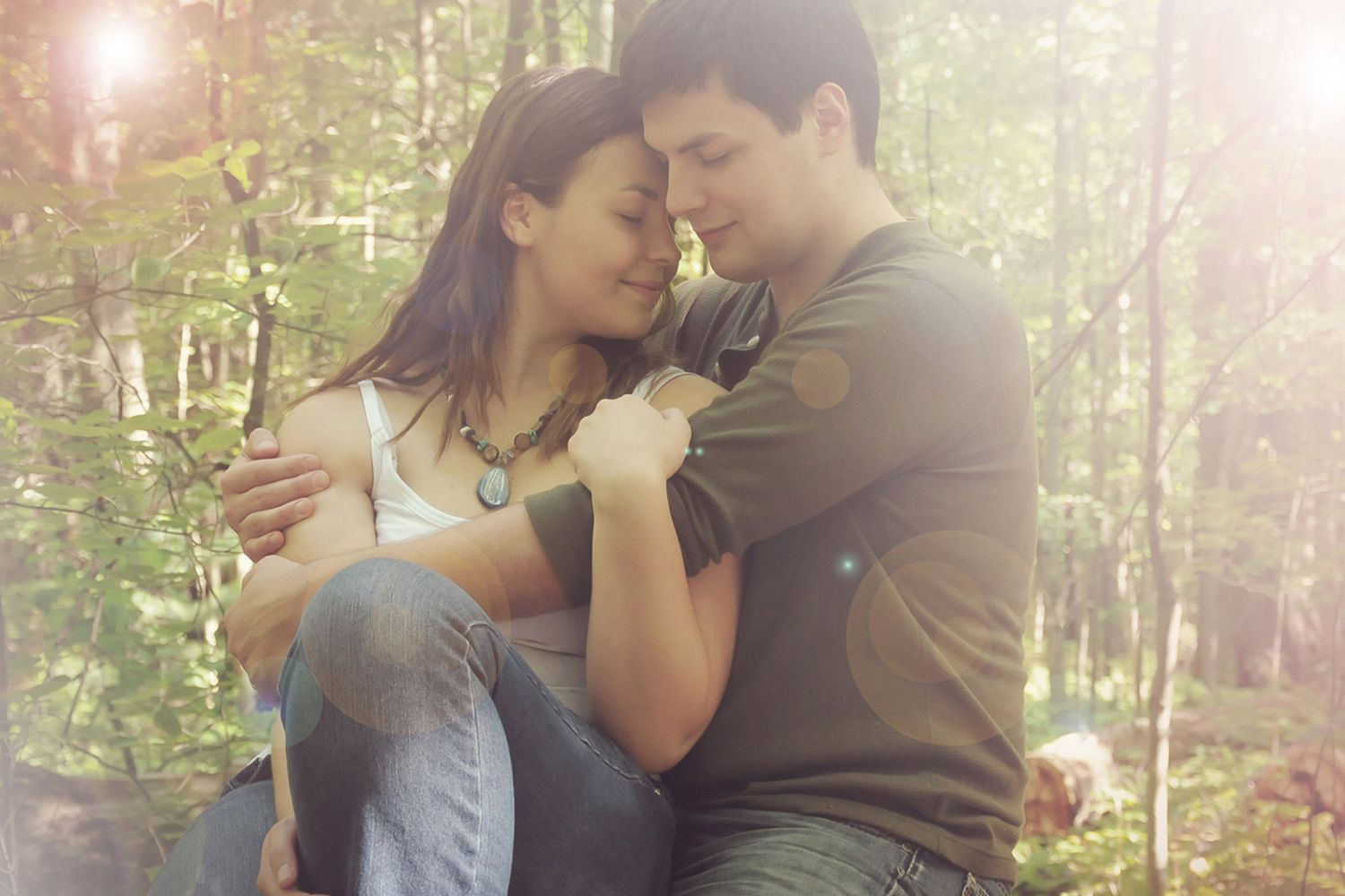 A romantic couple sharing an intimate moment in a sunlit forest setting.