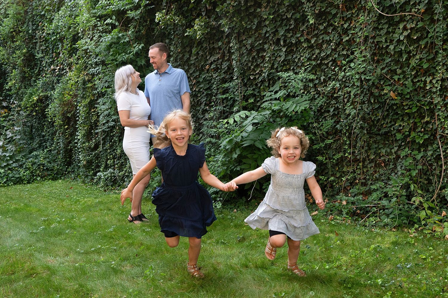 Family playing and running together in a lush green garden setting during a summer day.