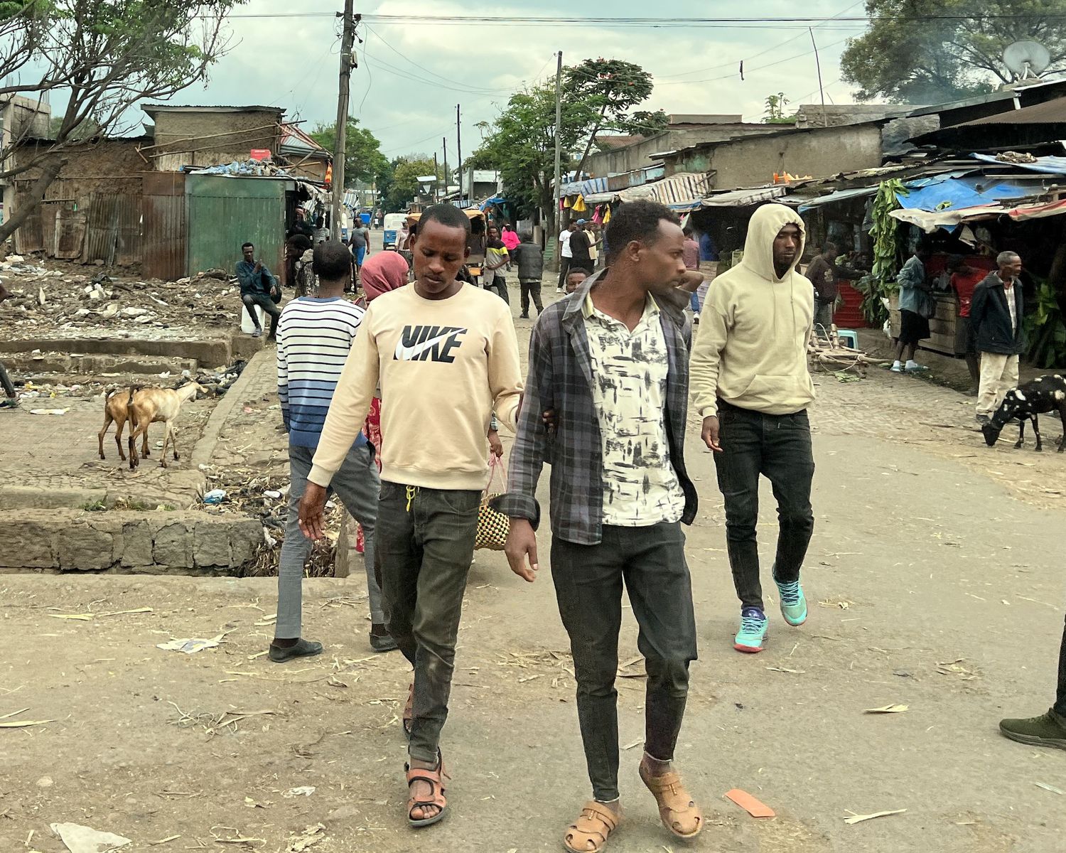 People walking through a busy marketplace with dirt paths and simple structures.