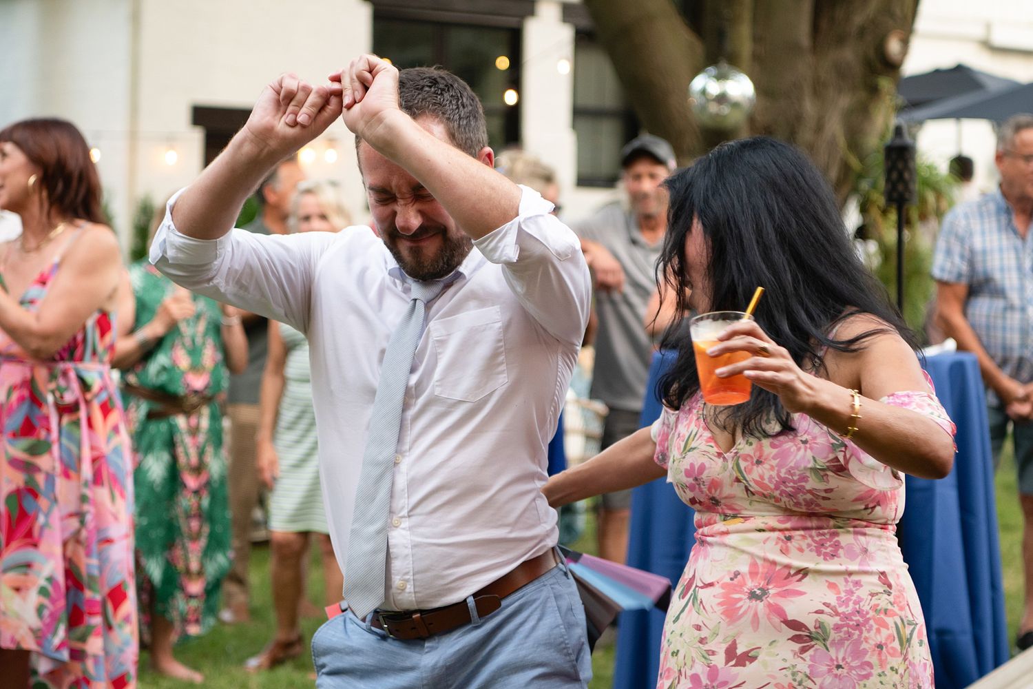 Party guests in summer attire dance and celebrate at an outdoor garden event.