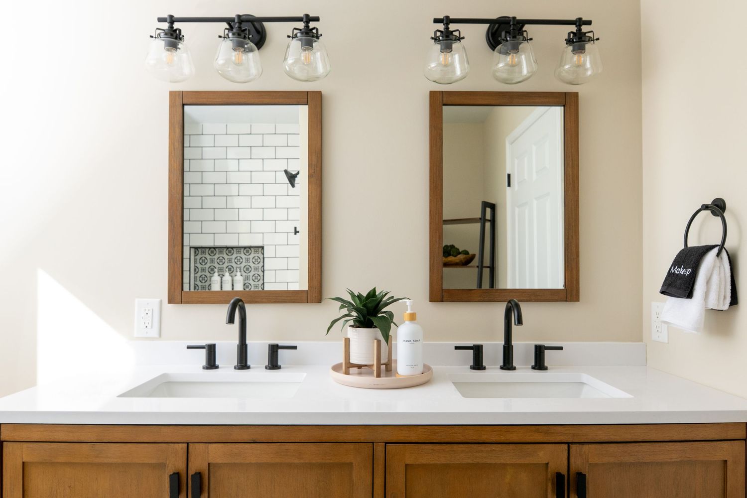 Modern farmhouse double vanity bathroom with wood cabinets, white countertop, black fixtures, subway tile, and framed mirrors.