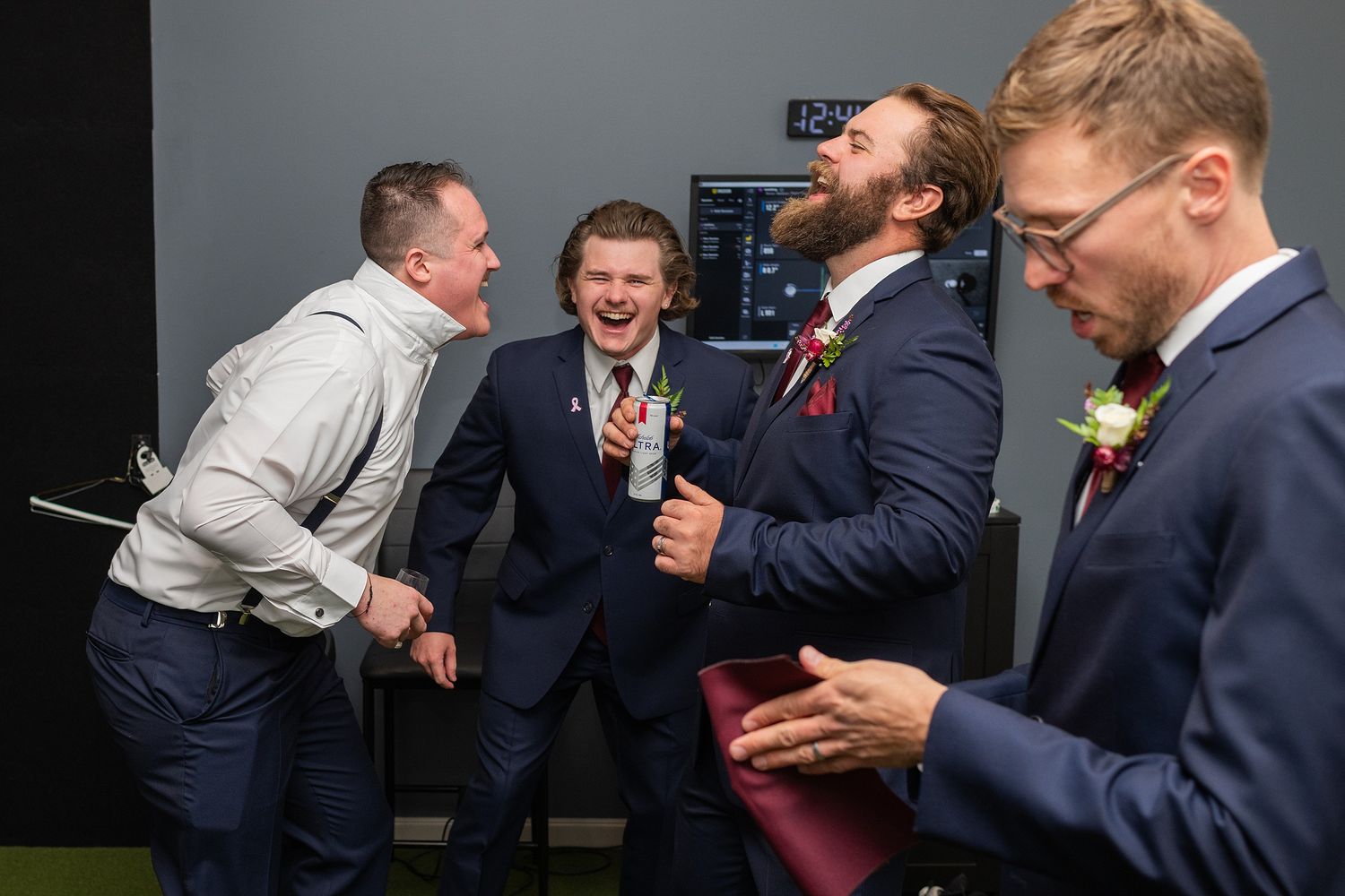 Four groomsmen in navy suits laughing and celebrating together at a wedding reception.
