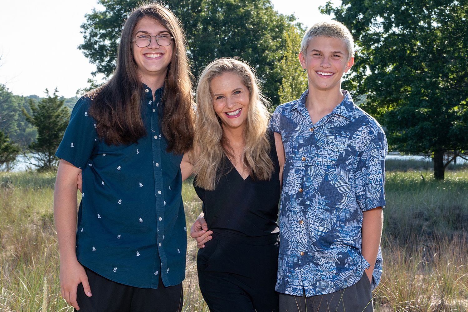 Three young people pose together outdoors in casual summer attire against a natural background.