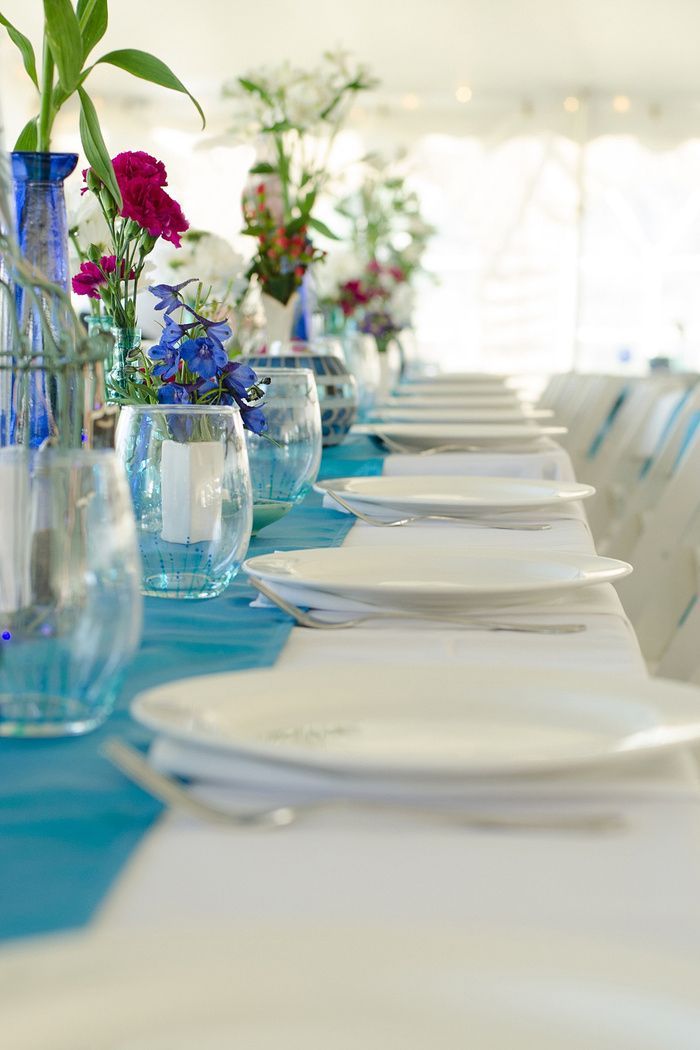 Elegant wedding table setting with blue runners and glass vases filled with colorful flowers.