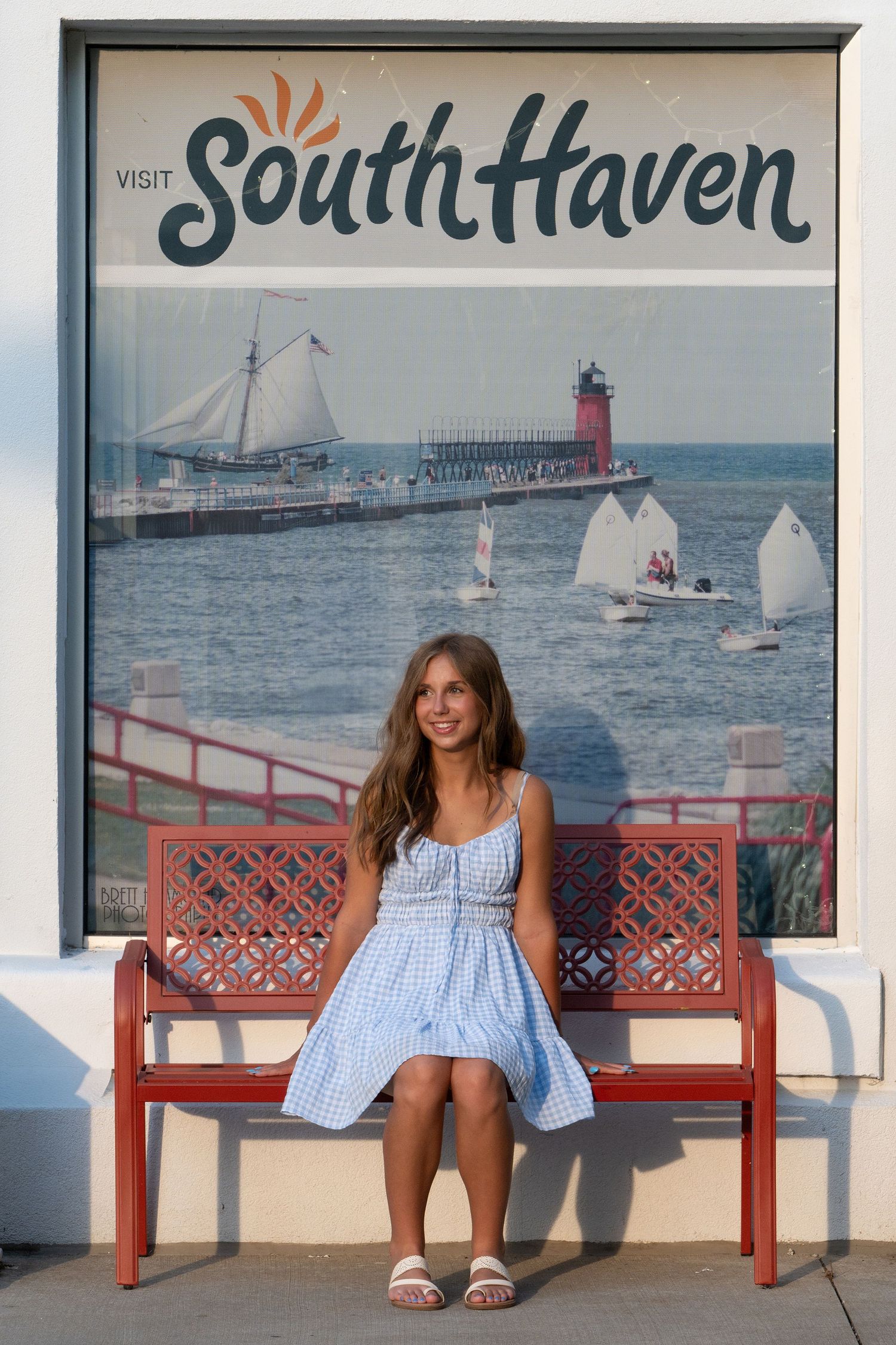 A seaside photoshoot on red benches with South Haven lighthouse and sailboats in the background.