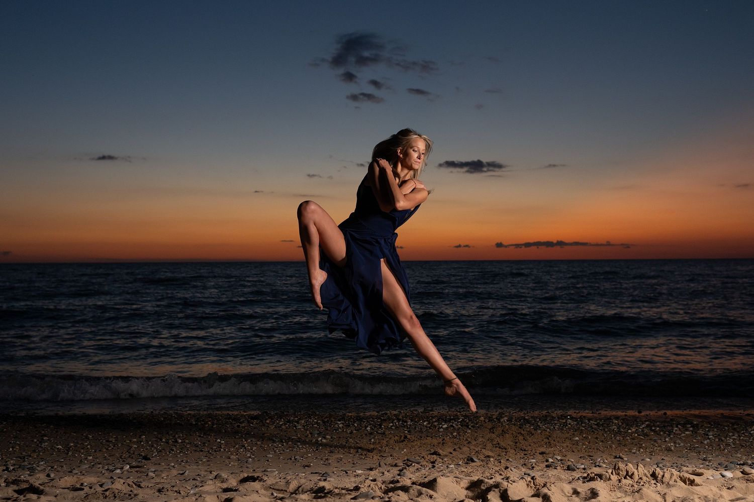 Dynamic leap captured against darkening sky during beach dance performance at dusk.