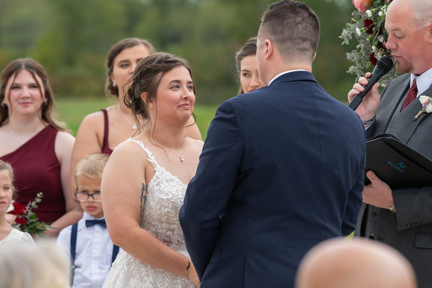 Bride and groom exchange vows at outdoor wedding ceremony surrounded by wedding party.
