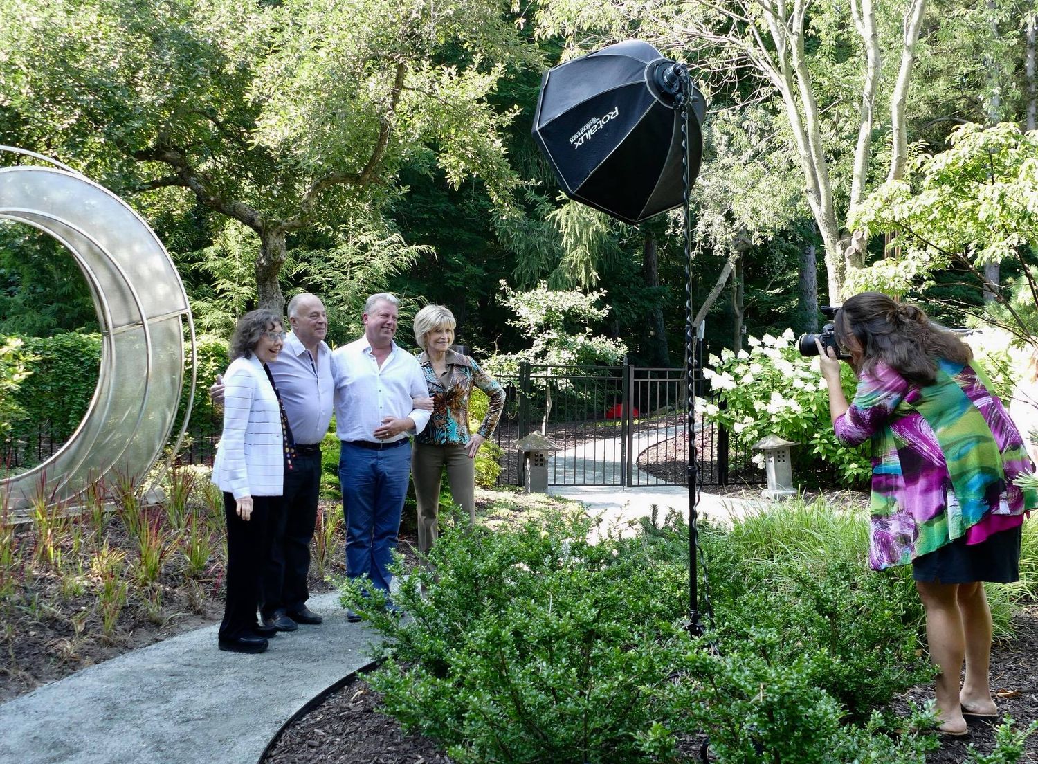 Outdoor photo shoot setup in a garden with lighting equipment and people gathered.