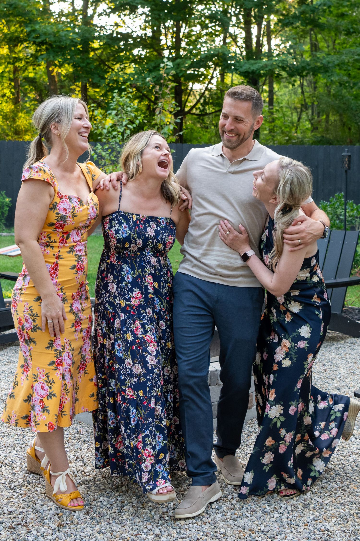 Group wearing floral dresses sharing genuine laughter in an outdoor garden setting.