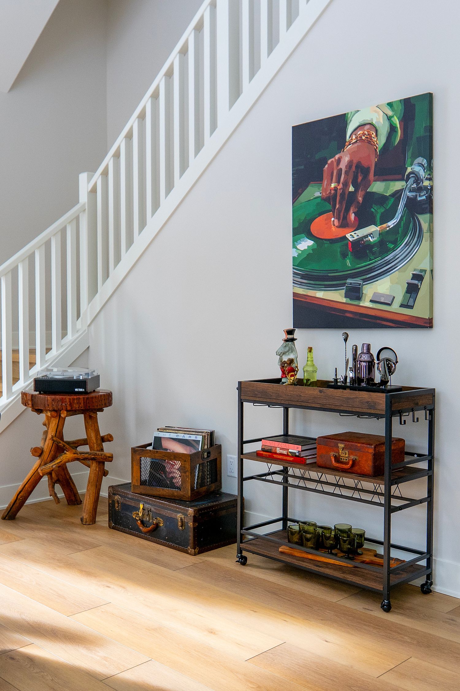Under-stair space decorated with vintage suitcases and colorful wall art on hardwood floors.